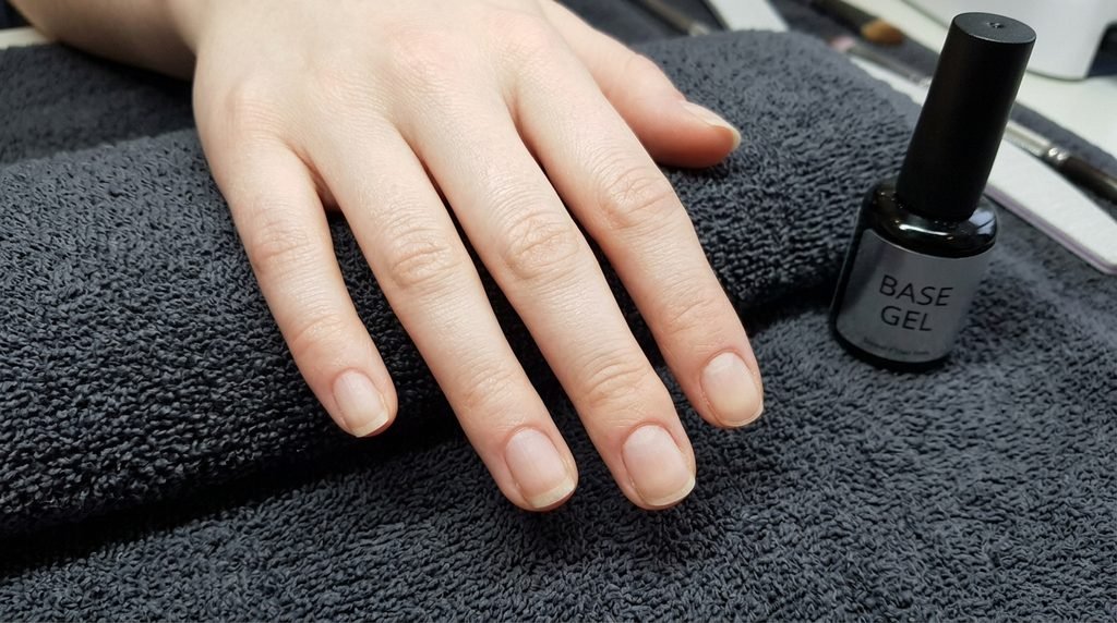 Prepped natural nails on an 18-year-old pale female hand ready for gel polish application on a dark grey towel.