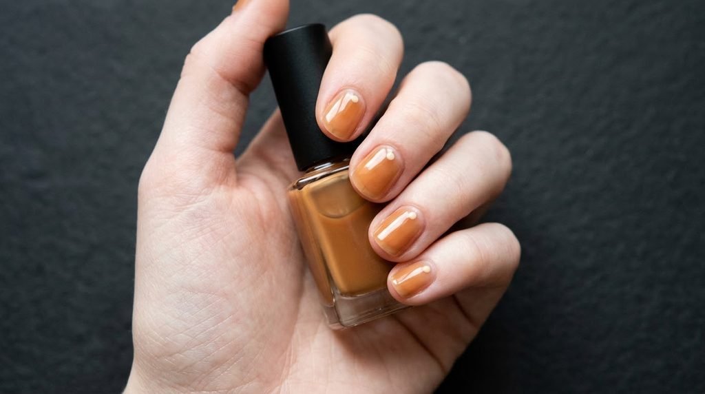Short natural nails with sheer caramel jelly polish on a female hand with very white skin tone.