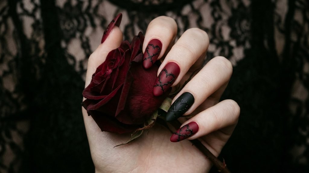 Goth valentines nails held against a dark red rose by an 18-year-old female hand.