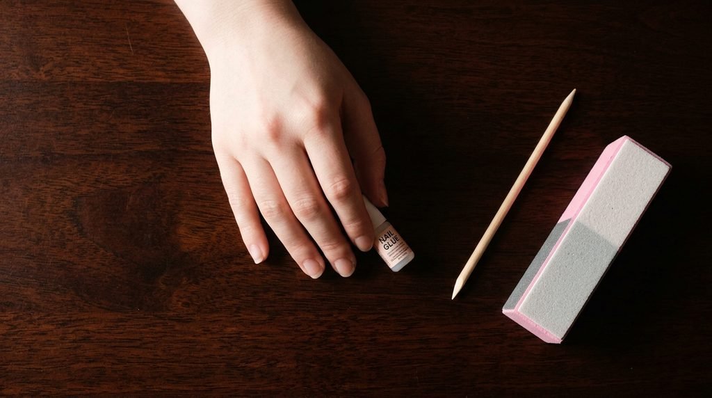 Female hand with very white skin arranging nail prep tools on a dark mahogany surface.