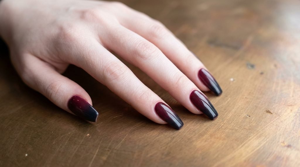 Wine red to jet black gradient ombre on coffin nails displayed over a polished bronze surface.