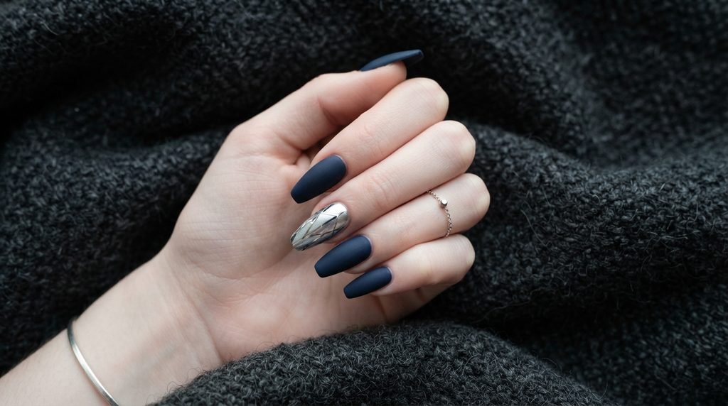 Top-down view of an 18-year-old female hand with white skin resting on a charcoal blanket, featuring matte navy coffin nails with silver geometric art.