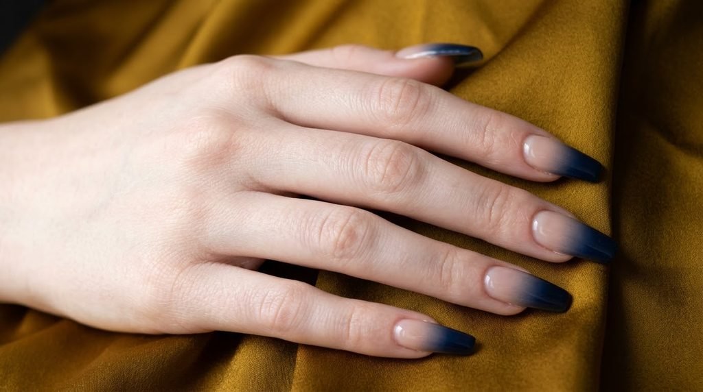 Midnight blue ombre coffin nails on an 18-year-old female hand with very white skin tone over mustard yellow silk fabric.