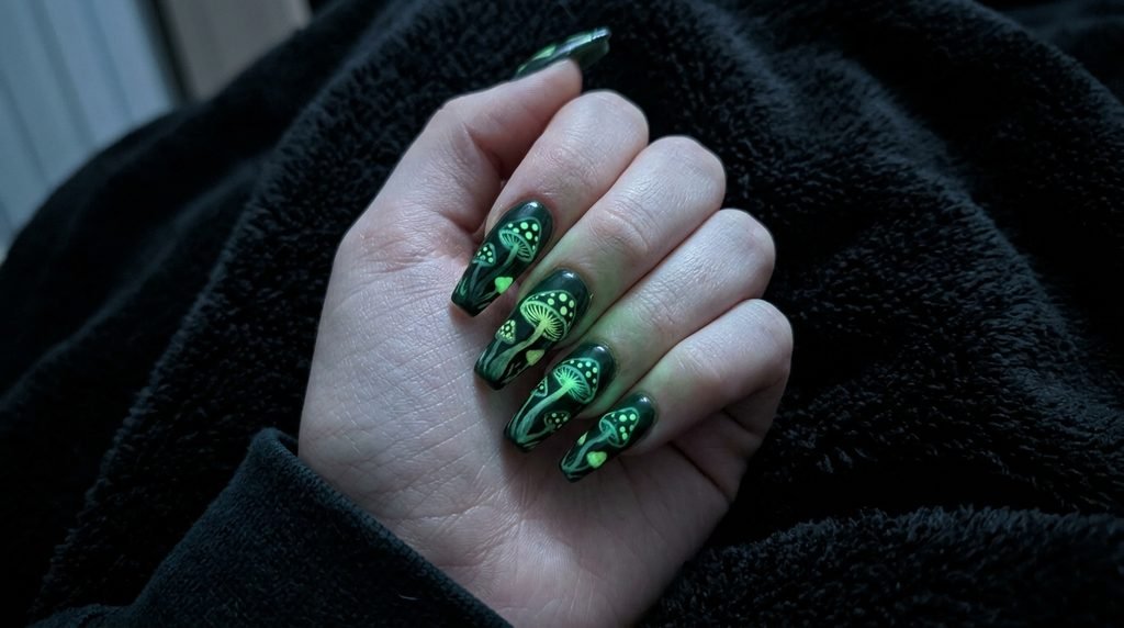 Glow in the dark green mushroom nail art glowing in dark lighting on an eighteen year old hand with white skin.