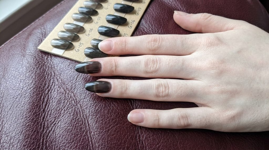 Sheer black glass nails on an 18-year-old female hand shown over maroon leather.