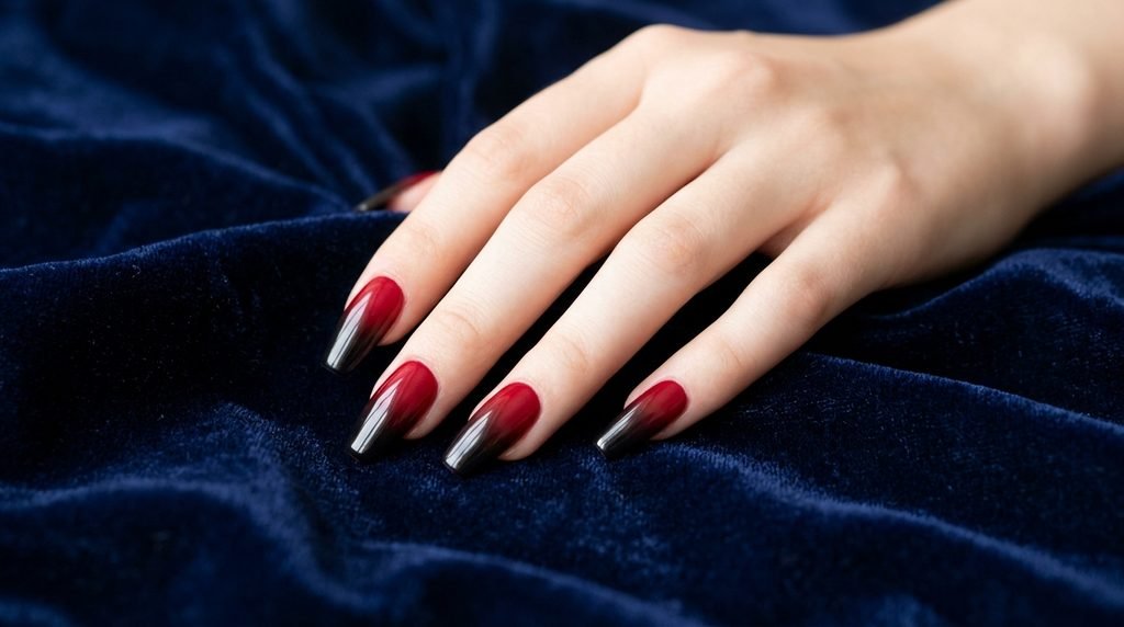 Red to black ombre coffin nails on an 18-year-old female hand over navy backdrop