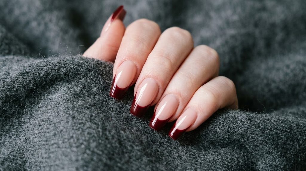 Oxblood red French tips on nude coffin nails held against dark charcoal cashmere fabric.