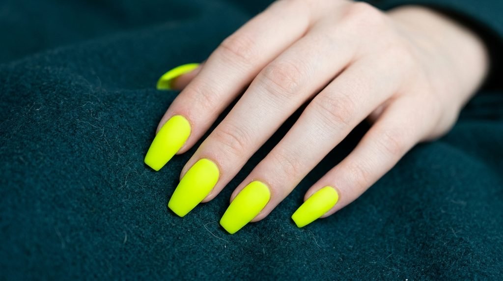 Extreme macro view of an 18-year-old hand with very white skin showing velvety matte neon green coffin nails on dark teal.