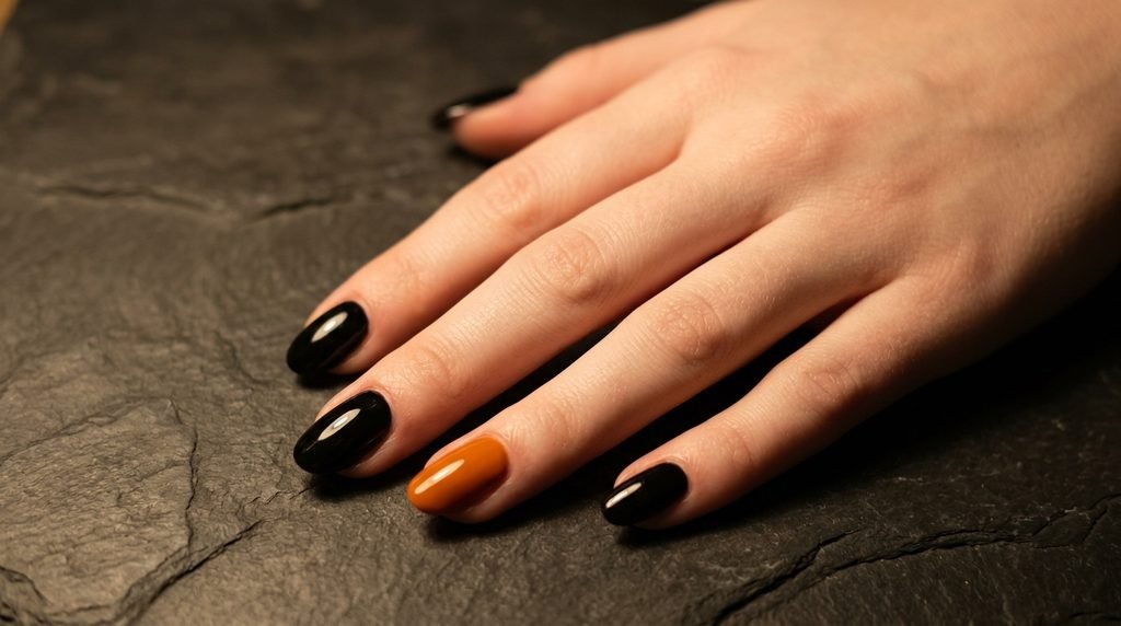 Close-up of an 18-year-old female hand with very white skin featuring glossy black and dark burnt orange oval nails on a slate background.