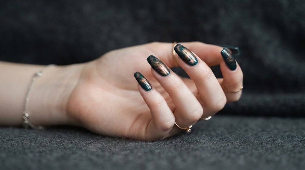 Detailed view of a galaxy accent nail with bronze chrome swirled into dark teal on white skin