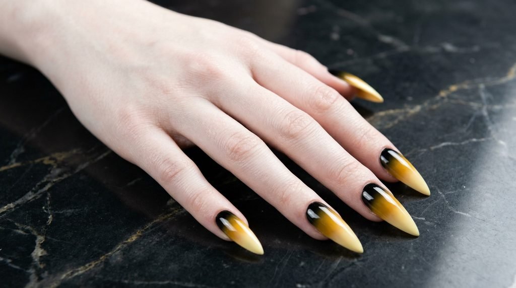 Long stiletto nails showing a range of yellow shades and black on an 18-year-old female hand with pale skin.