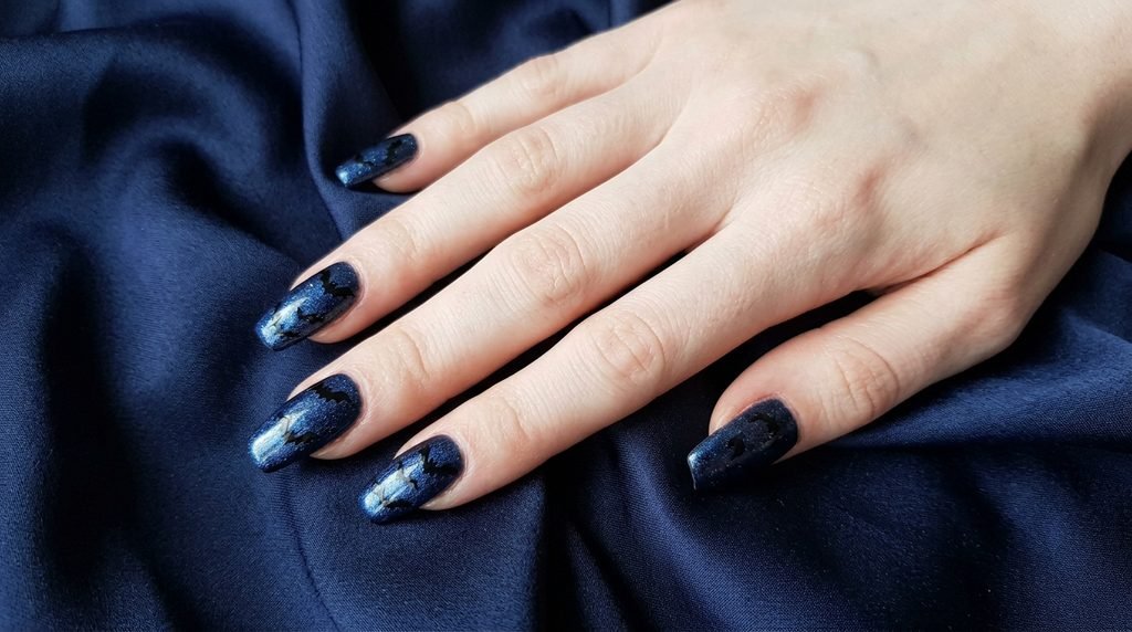Coffin nails with midnight blue shimmer polish and black flying bat art on smooth white skin.