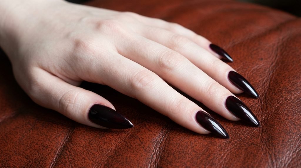 Glossy plum noir stiletto nails on an 18-year-old female hand with very white skin tone over burnt orange leather.