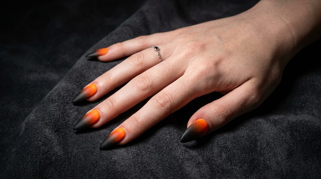 Sharp stiletto nails with orange aura cores and matte black tips on dark charcoal suede