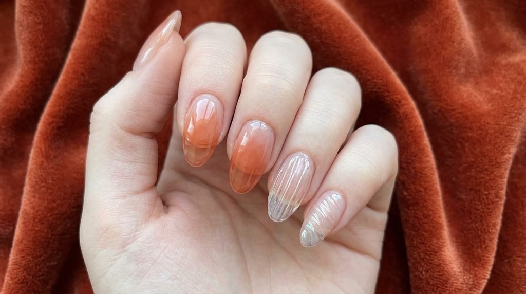 Hybrid manicure showing smooth syrup gel and 3D ribbed glass accents on light skin over terracotta velvet.