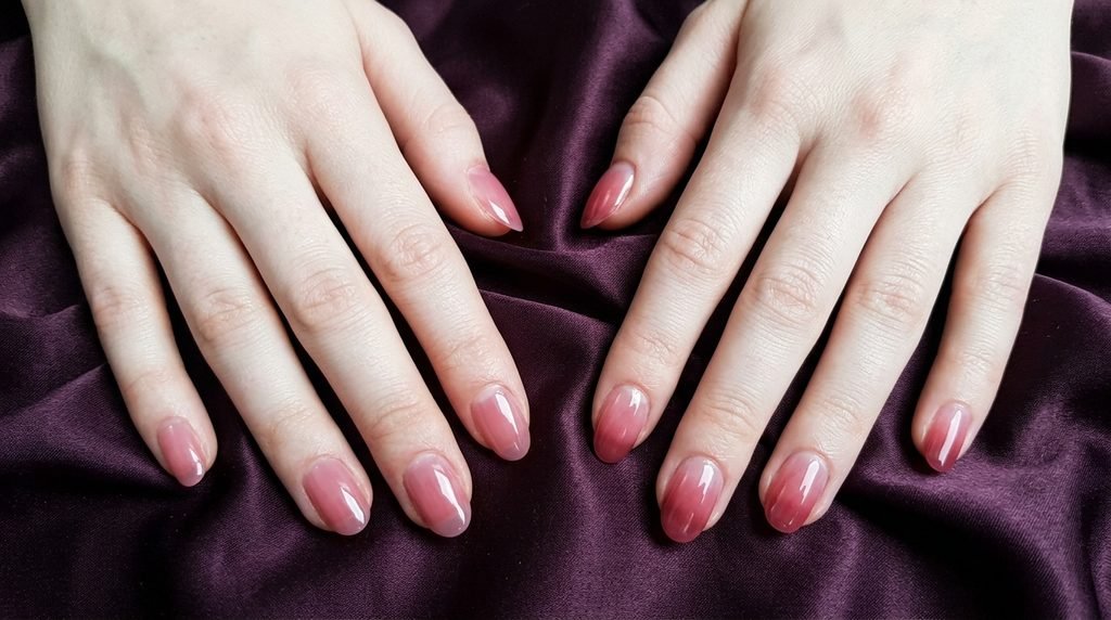 Two hands with white skin displaying the visual difference between jelly and syrup polish against plum satin.