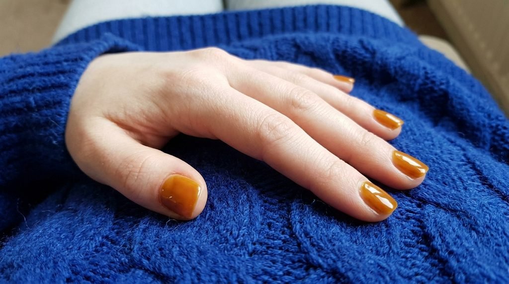 Short squoval syrup nails in warm honey brown on fair skin against dark royal blue sweater.