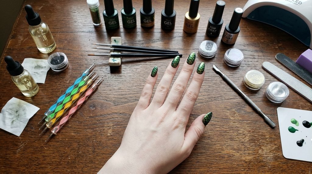 Nail art tools and green snake scale nails on a pale female hand over dark oak background.