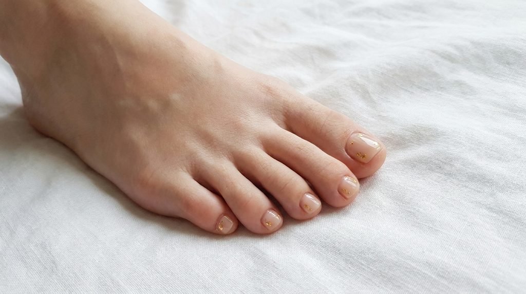 Short toenails with smooth fair skin featuring subtle gold foil accents over a nude base.