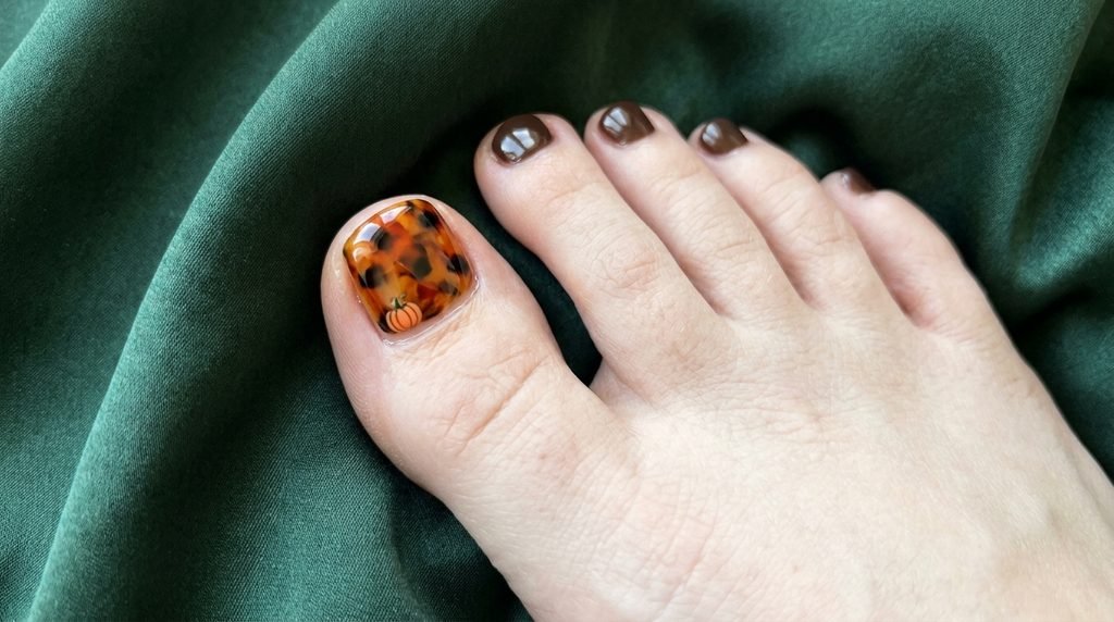 Tortoiseshell big toenail pattern with a micro orange pumpkin outline on white skin over dark forest green satin.