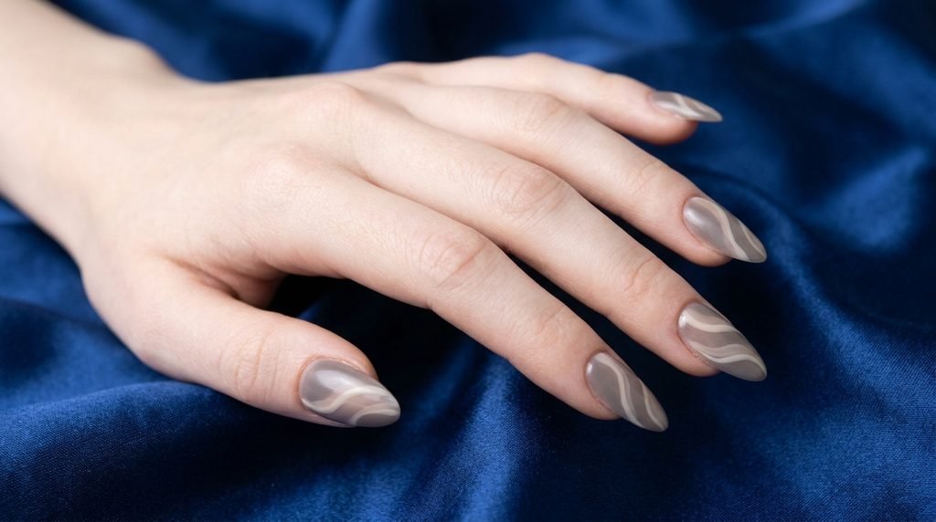 Cashmere nails with smoky taupe swirls on long almond nails over sapphire blue backdrop.