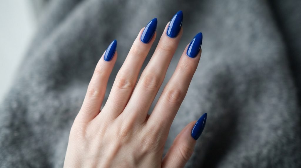 Close-up of brilliant high-gloss sapphire blue cream nails on an 18-year-old female hand, fingers splayed.