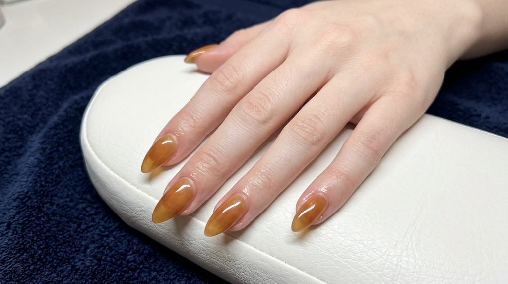 Freshly manicured almond syrup nails on a light-skinned hand resting on a white salon towel.