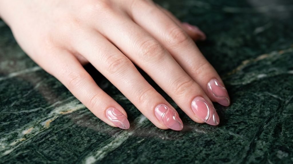 Rose pink ribbed glass almond nails on an 18-year-old female hand with very white skin against dark emerald marble.