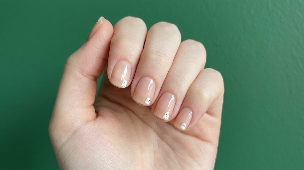 Short squoval nails with clear nude polish and micro white ghost accents on smooth white skin.