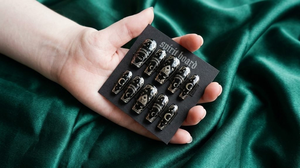 Female hand with white skin holding pre-designed spirit board press-on nails over dark silk.