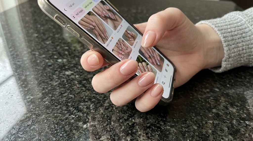 A manicured hand with smooth white skin holding a phone over a dark granite background.