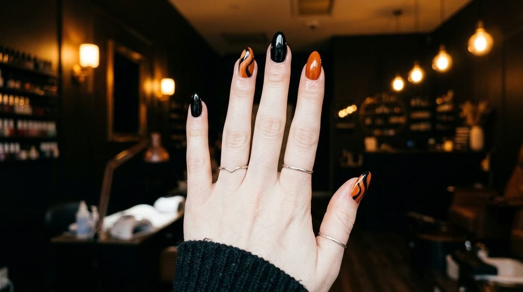 Completed dark  orange and jet black almond manicure on an 18-year-old pale female hand inside a salon.