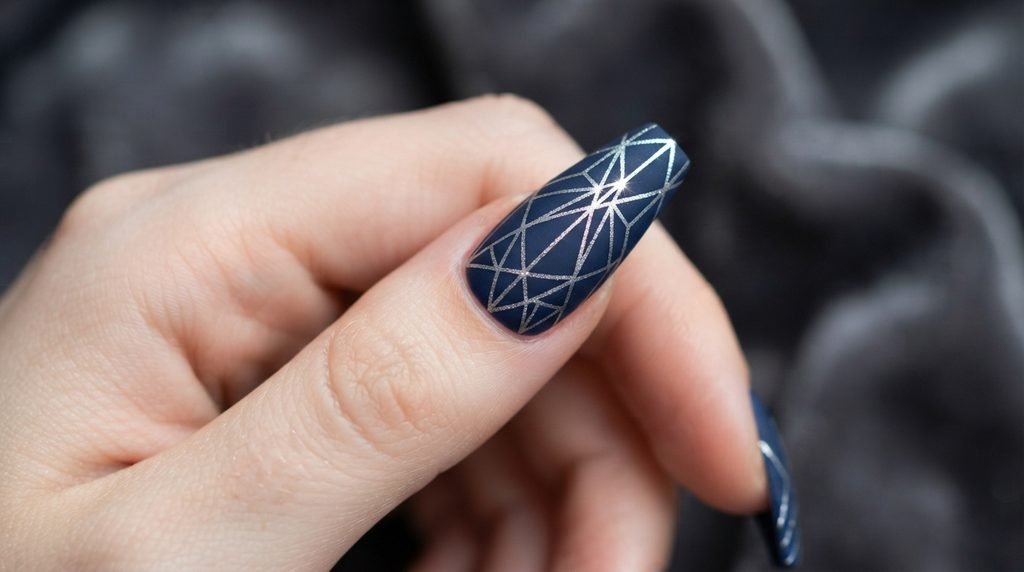A macro close-up of a single long coffin nail on an 18-year-old woman with very white skin. It features a matte navy base with precise, intricate silver metallic geometric crystalline art.