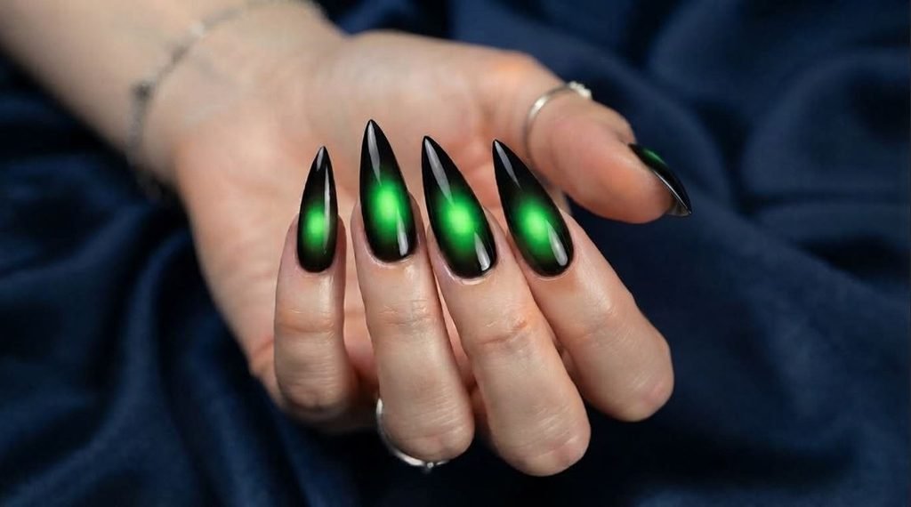 Stiletto nails displaying vibrant green aura centers with glossy black borders on sapphire silk.