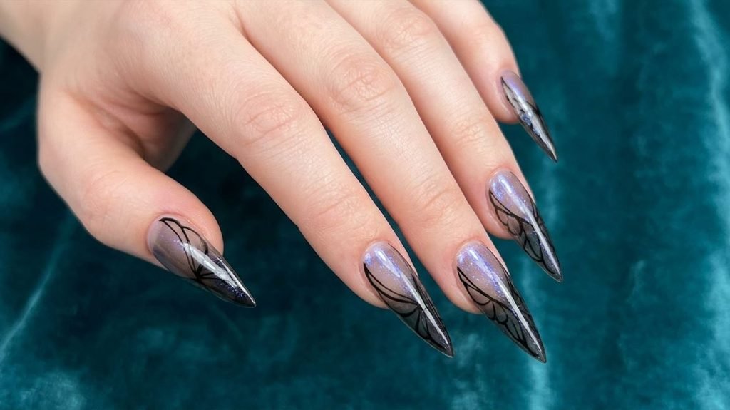 Close-up of three sharp stiletto nails with a smoky gradient and delicate, flowing black linework forming abstract moth-wing structures, dusted with iridescent pigment.